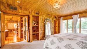 Ein Holzhütten-Innenraum mit einem großen Bett, einer Chandelüster und Blick durch die geöffnete Tür.