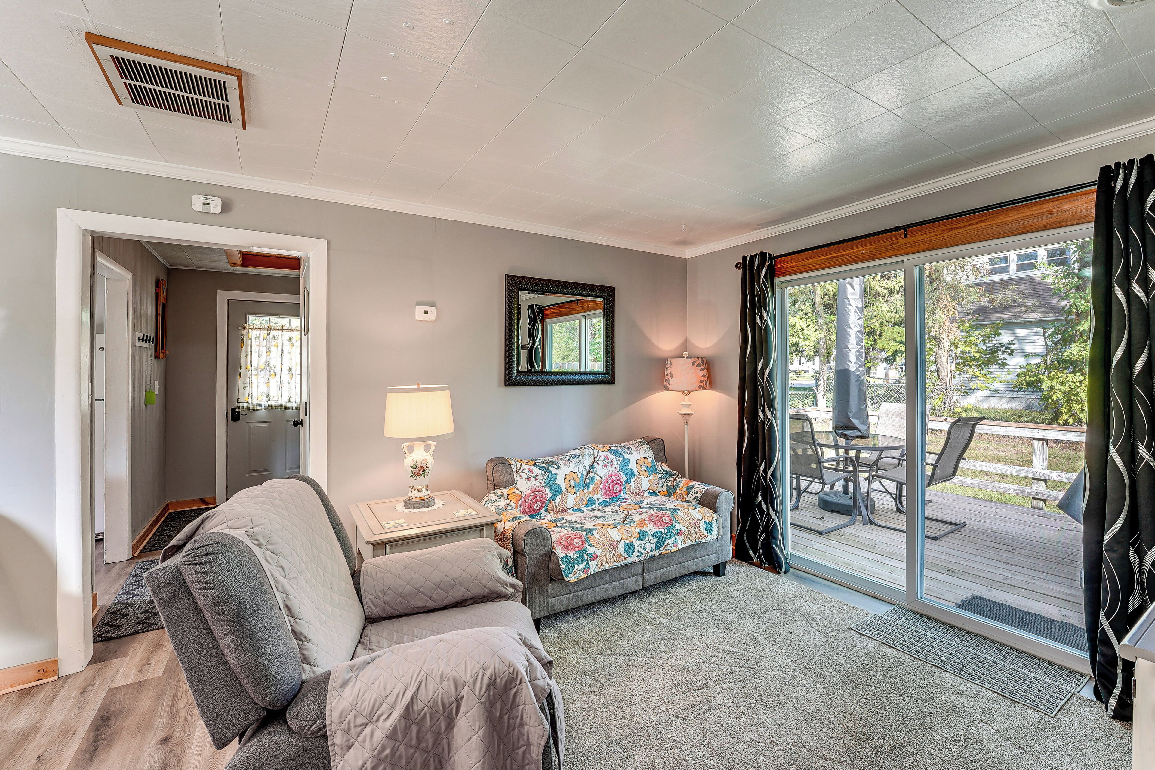 A cozy living room with a sofa, a side table with a lamp, and a view of the outdoor deck through large sliding glass doors.