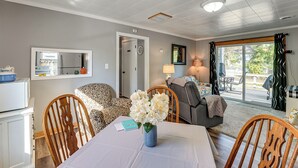 A dining area with a table set for two, a vase with flowers, and a view of the outdoors through a sliding glass door.