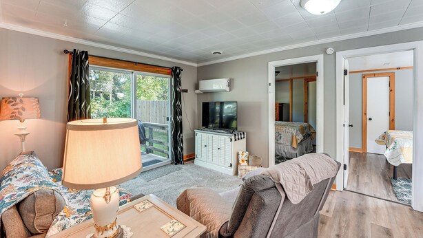 A cozy living room with a sofa, a table with a lamp, a television, and a sliding glass door leading to a balcony.