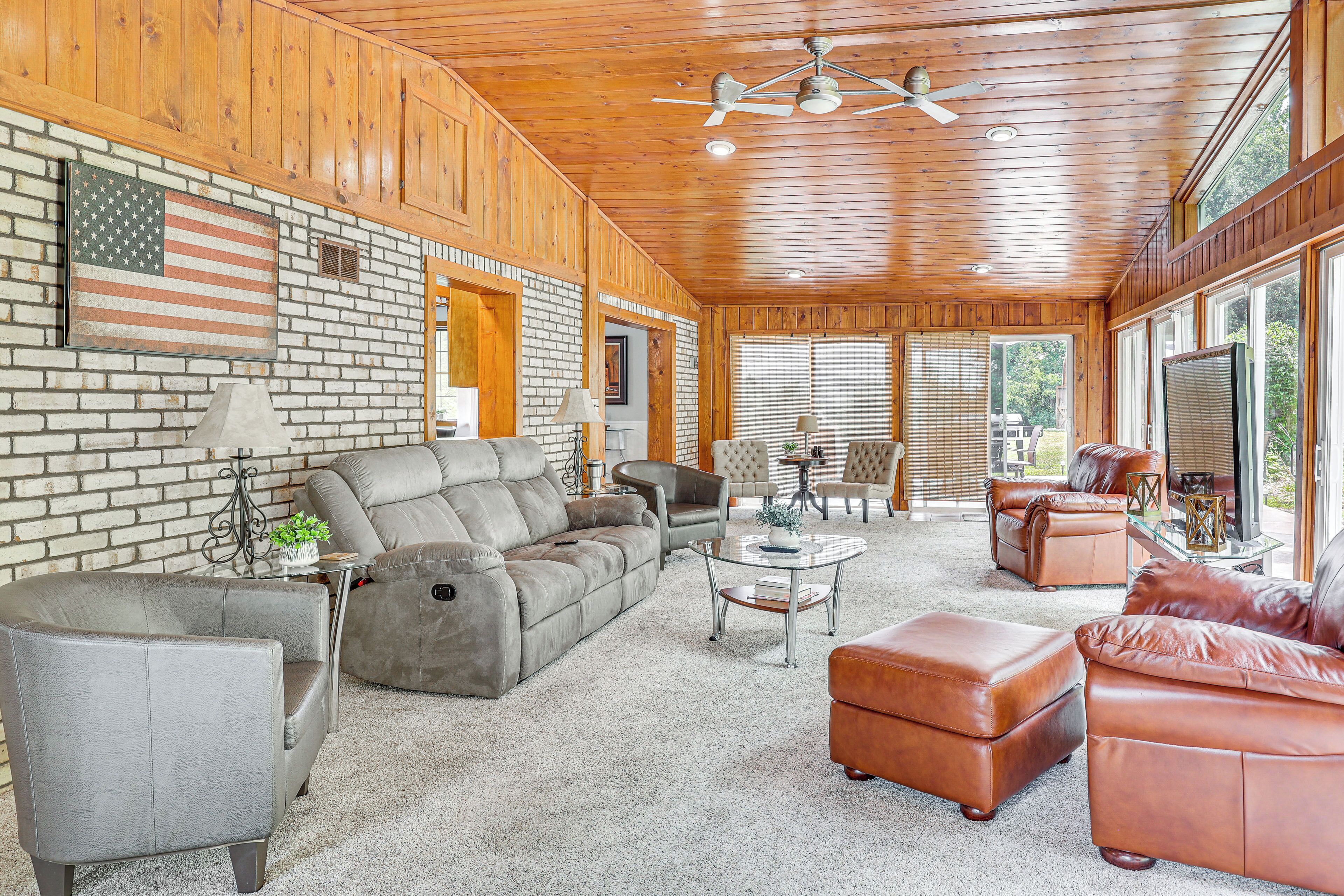 A spacious living room with a large sectional sofa, leather armchairs, and a glass coffee table.