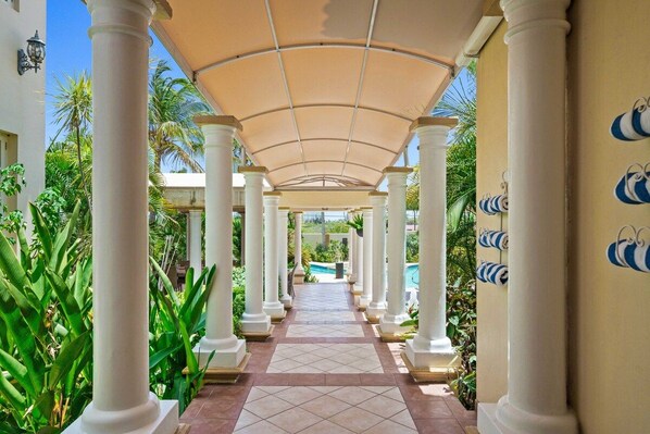 A covered walkway with columns, a tiled floor, and a pool in the background.