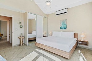 Ein Schlafzimmer mit einem großen Bett, einem Deckenventilator, einer Klimaanlage, einem Nachttisch mit einer Lampe und einem Spiegel an der Wand.