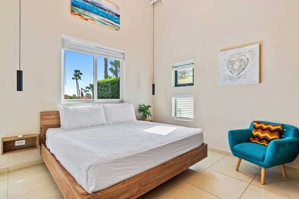 A bedroom with a wooden bed, a window with blinds, a blue armchair, and a wall-mounted heart-shaped decoration.