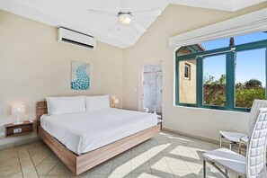 Un dormitorio con cama, mesitas de noche, ventilador de techo, aire acondicionado, ventana con vistas y una silla.