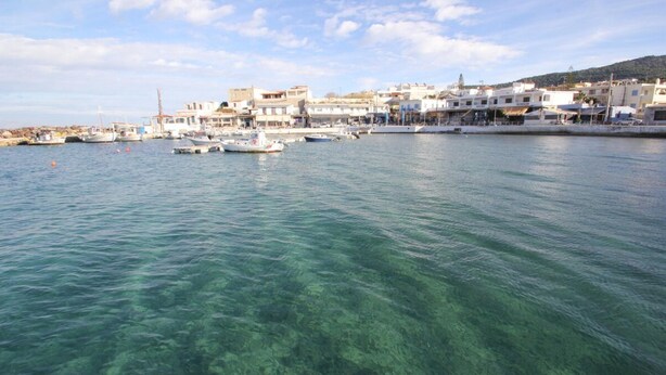 Une ville côtière aux eaux limpides, où des bateaux sont amarrés et où les bâtiments s’alignent le long de la côte.