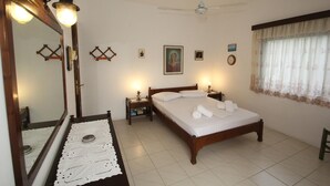 Une chambre à coucher avec un lit en bois, un grand miroir, des lampes de chevet, un ventilateur de plafond et une fenêtre avec des rideaux.
