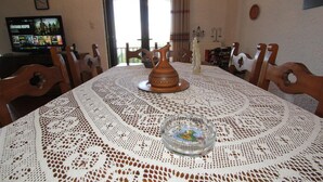 Une table à manger recouverte d’une nappe en dentelle blanche, agrémentée d’un objet décoratif central et d’un cendrier en verre.