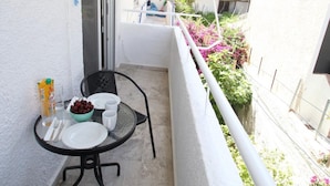 Un balcone con un tavolo apparecchiato per due persone, una sedia e una piccola ciotola di frutta.