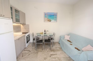 Une cuisine de taille réduite comprenant une table à manger, un canapé et un tableau représentant une scène de plage.