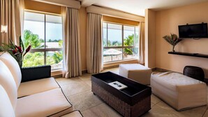 A modern hotel room with a sofa, a coffee table, and a TV. Large windows offer a view of the outdoors. - Gaia Collection Hotels - Adults only (Quepos)