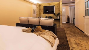 A hotel room with a large bed, a sofa with cushions, a flat-screen TV mounted on a stone wall, and a hallway leading to a door. - Gaia Collection Hotels - Adults only (Quepos)