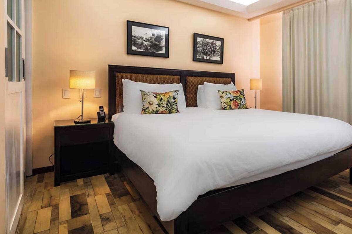 Habitación de hotel con una cama grande, dos mesitas de noche, un teléfono y dos cuadros en la pared.
