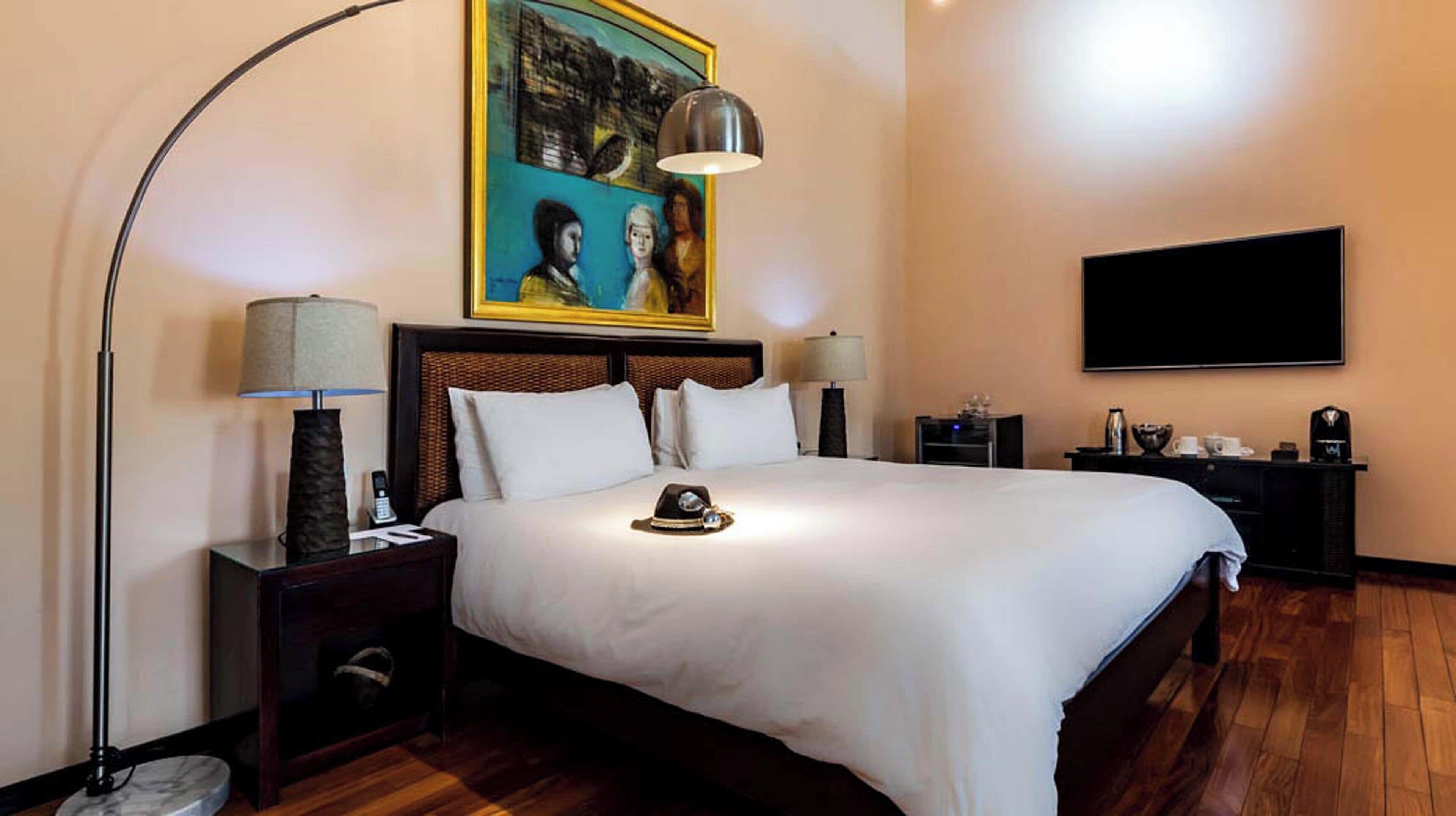 A hotel room with a large bed, two bedside lamps, a flat-screen TV, and a painting on the wall.