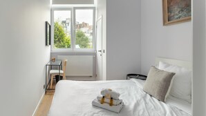 A hotel room with a large bed, a small desk, and a window with a view of buildings and trees. - Brussels Toison D'or (Brussels)