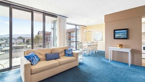 A modern living room with a beige sofa, a dining table with chairs, and large windows offering a city view. - Sand & Sea (316) Marine Dream-Beachview with Pool (Seaside)