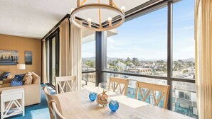 A hotel room with a large window, a dining table with chairs, a chandelier, and a view of the city. - Sand & Sea (316) Marine Dream-Beachview with Pool (Seaside)