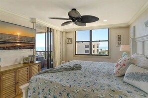 A bedroom with a large bed, a ceiling fan, a view of the ocean, and a balcony.