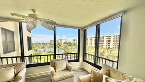 Een balkon met uitzicht op een hotelcomplex, een plafondventilator en een zithoek met gestreepte kussens.