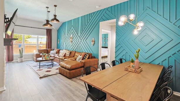 A modern living room with a teal accent wall, leather sofa, wooden dining table, and pendant lighting.
