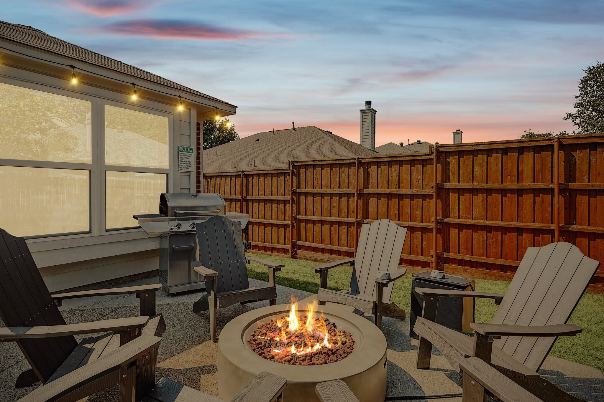 Un jardin avec un foyer, des sièges d’extérieur, un barbecue et une clôture en bois.