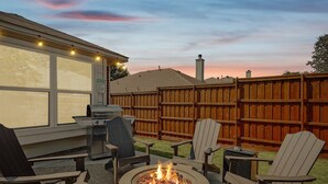 A backyard with a fire pit, outdoor seating, a grill, and a wooden fence.