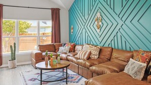 A cozy living room with a brown leather sofa, a round coffee table, and a teal accent wall with geometric patterns.