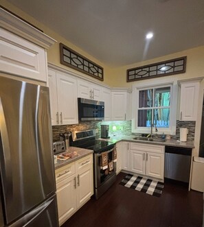 A kitchen with white cabinets, stainless steel appliances, a microwave, and a window with curtains.