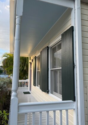 A porch with a white railing, a covered area, and a view of the street.