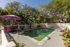 Une piscine dotée d’une terrasse en bois, entourée d’une clôture blanche et d’arbres.