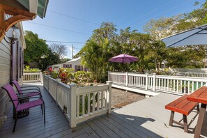 Une terrasse en bois avec une balustrade blanche, un parasol violet et une table en bois.