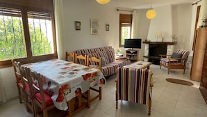 Ein gemütliches Wohnzimmer mit einer Couch, Sesseln, einem Esstisch und einem Fernseher.