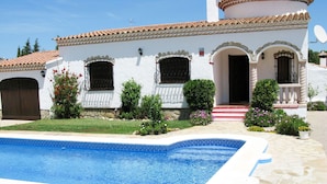 Eine weiße Villa mit Swimmingpool, Ziegeldach und Garten mit Blumen und Sträuchern.