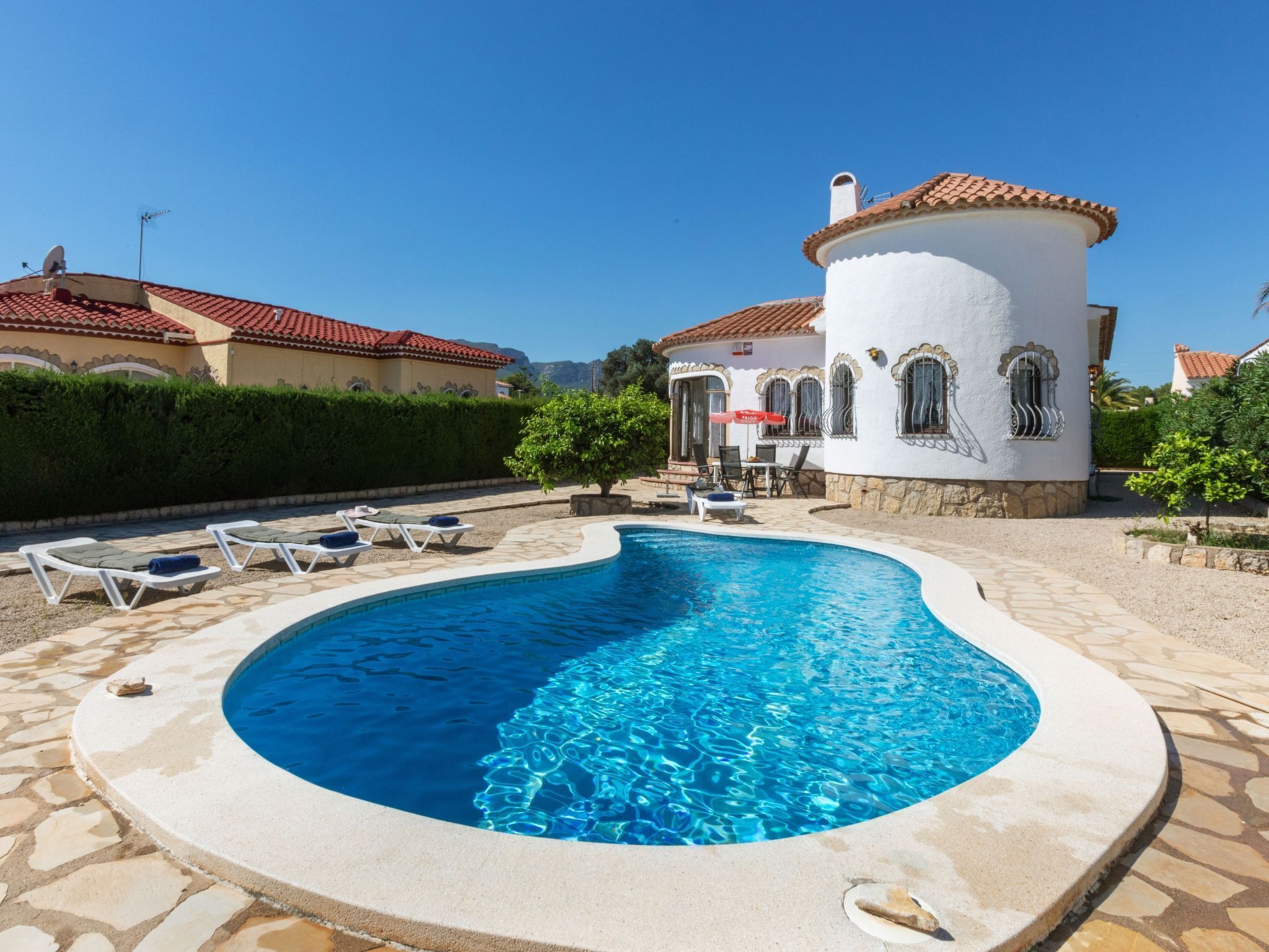 A swimming pool with lounge chairs, a white building with a red-tiled roof, and a stone pathway.
