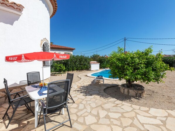 A patio with a table and chairs, a pool, and a small tree.