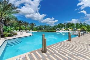 A swimming pool with lounge chairs and umbrellas, surrounded by palm trees and a clear sky.