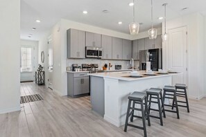 A modern kitchen with grey cabinets, stainless steel appliances, and a central island with bar stools.