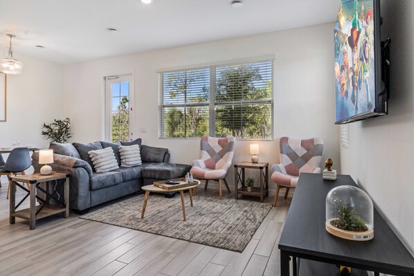 A modern living room with a grey sofa, a patterned armchair, a coffee table, and a TV mounted on the wall.