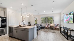 A modern kitchen with a central island, stainless steel appliances, pendant lighting, and a large window providing natural light. - Enhanced  Townhome! Minutes from Disney World! Resort Amenities! (Davenport)