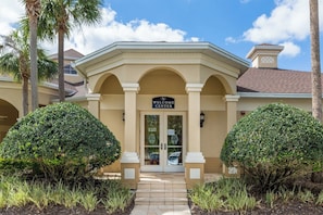 A building with a 'WELCOME CENTER' sign, a covered entrance, and symmetrical landscaping with two large bushes.