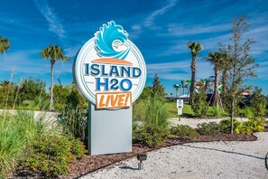 A sign for Island H2O with a wave design, surrounded by greenery and palm trees. - 3BR Margaritaville Resort Townhouse, Close to WDW! (Kissimmee)