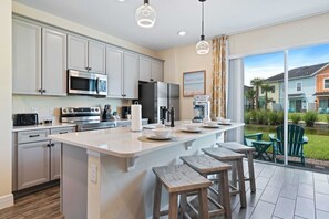 Modern, fully equipped kitchen featuring stainless steel appliances and cabinetry - Large island with a white marble countertop, seating for four, and stylish pendant lighting - Sliding glass door provides plenty of natural light with a scenic view - 3BR Margaritaville Resort Townhouse, Close to WDW! (Kissimmee)