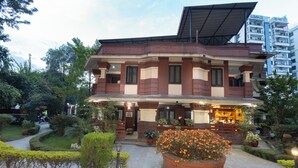A two-story building with a covered entrance and a garden area with potted plants and a large flower bed.