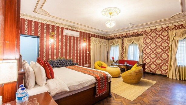 A hotel room with a large bed, two armchairs, a small table, and a chandelier.