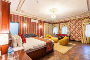 Una habitación de hotel con una cama grande, dos sillones, una mesita y una araña.