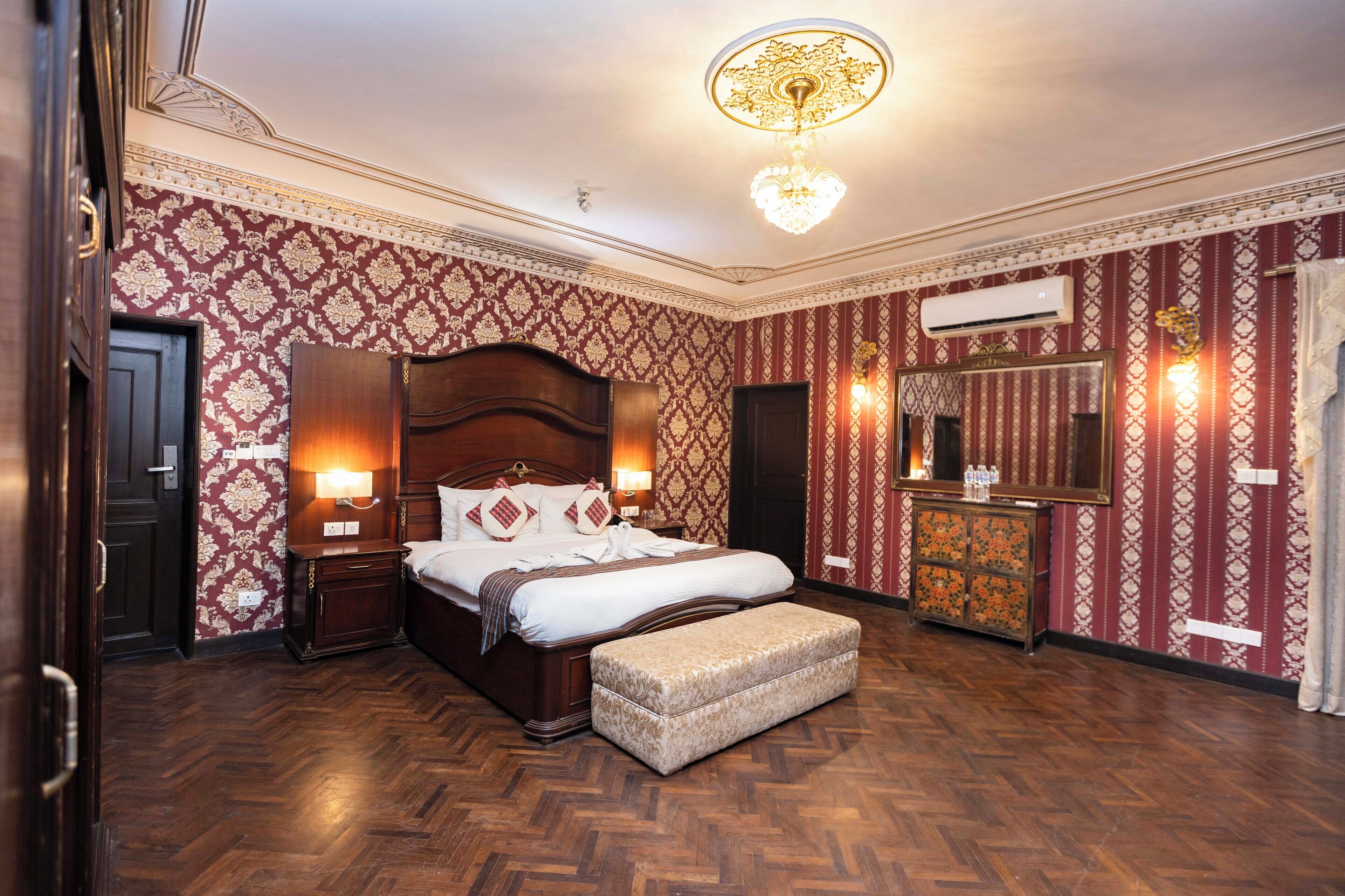 Habitación de hotel con una cama grande, cabecera de madera, mesita de noche con lámpara, cómoda y espejo.