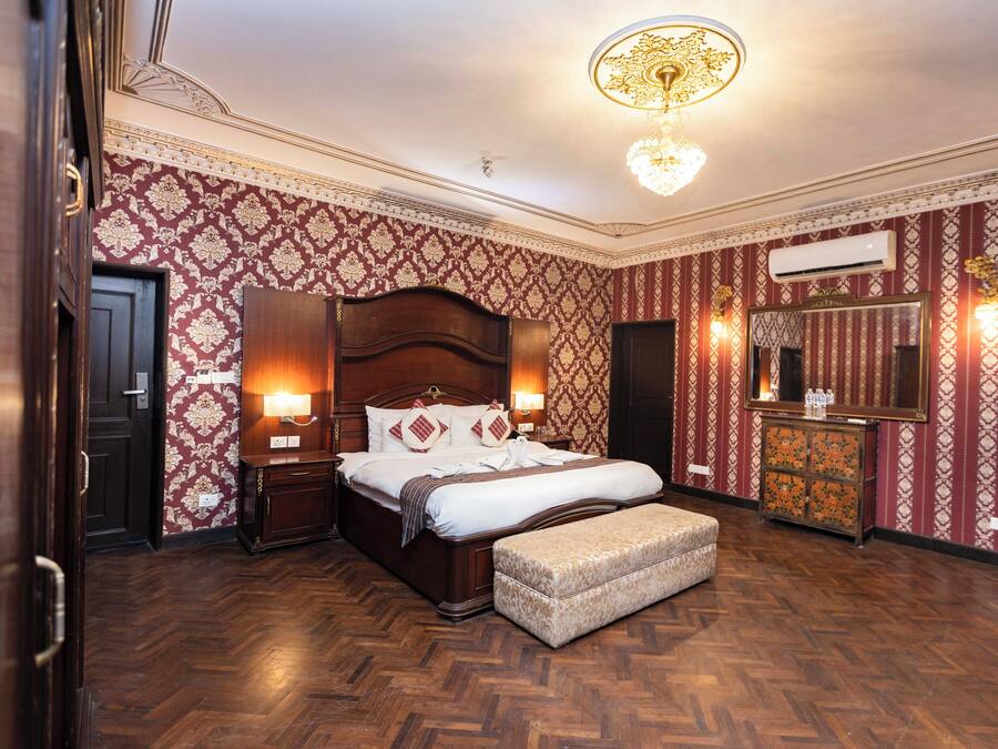Habitación de hotel con una cama grande, cabecera de madera, mesita de noche con lámpara, cómoda y espejo.