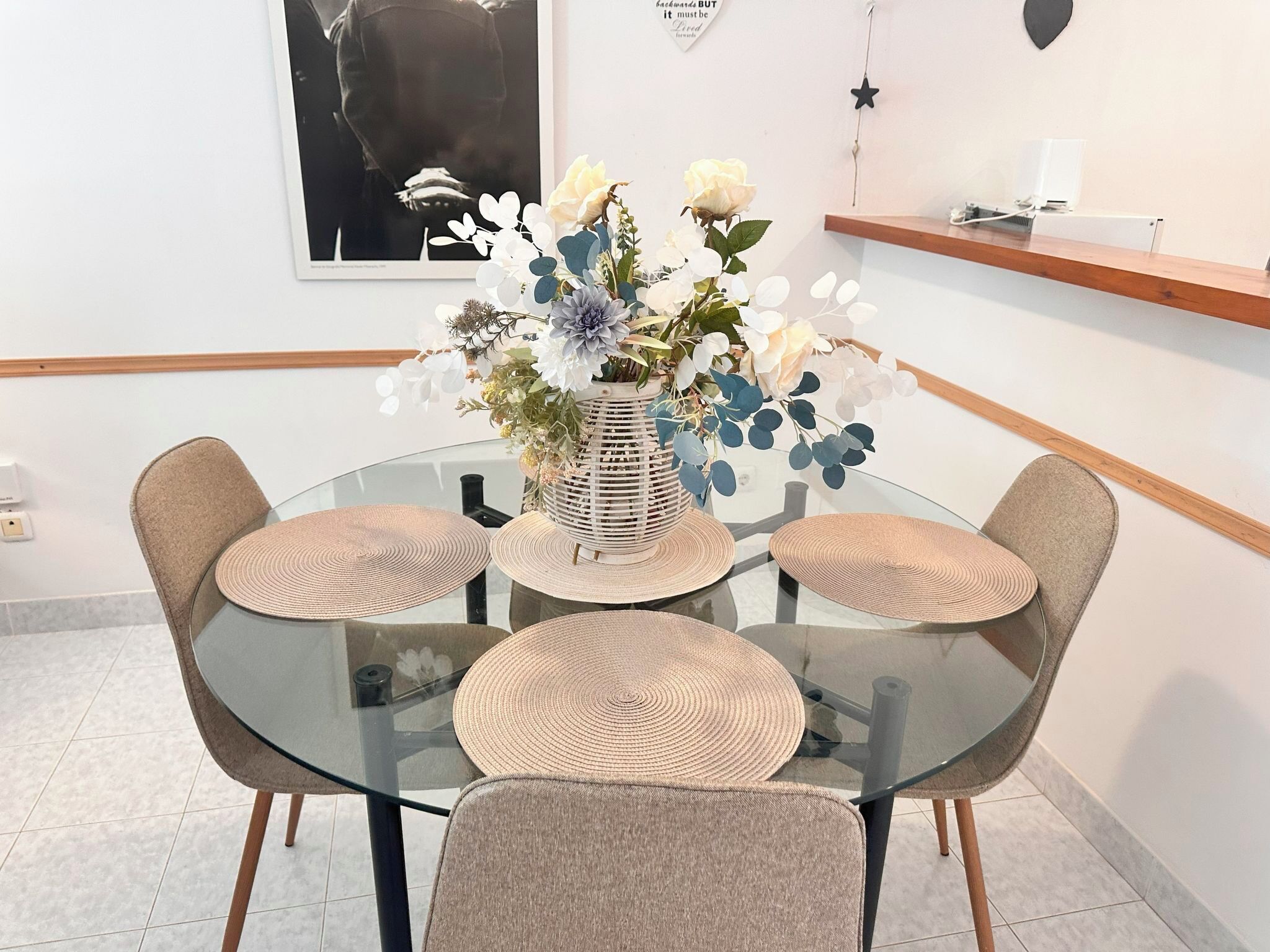 A round glass table with woven placemats and a vase of flowers.