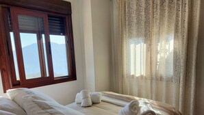 Une chambre d’hôtel avec un lit, deux oreillers, une fenêtre avec des stores et un rideau.