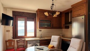 Une cuisine compacte avec des meubles en bois, un lave-linge encastré, un coin repas avec une table en verre et un coin salon avec une chaise et un canapé.